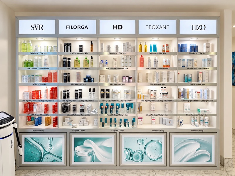 Vitrina iluminada de productos de cuidado de la piel, organizada por marca en columnas y por tipo de piel en filas.